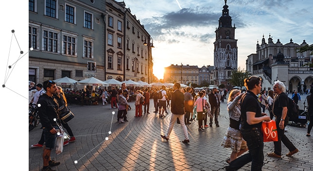 Une place en Europe remplie d’une foule de gens qui marchent et une terrasse de café avec des tables et des parasols