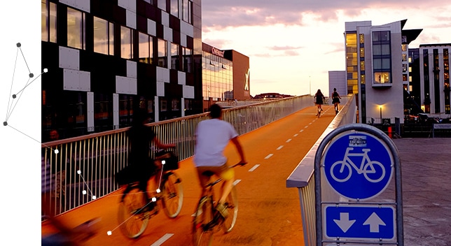 A bicycle bridge with 2 people riding bicycles and a bright blue traffic sign showing a bicycle and two arrows