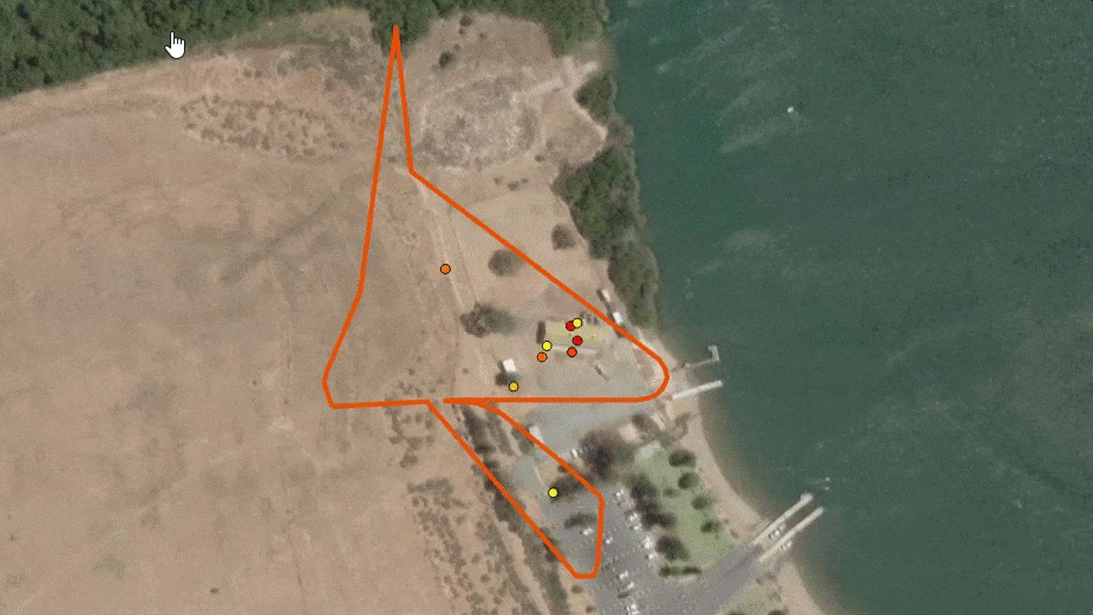 A satellite image showing a barren area next to a body of water, with orange polygon outlines and small red points marking locations for analysis