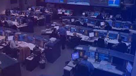 A large mission control center room with rows of desks and people working on computers