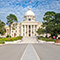 The Alabama State Capitol building with dramatic columns and a cupula on a slight, well-manicured hill 