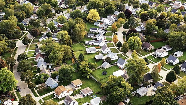 An aerial image of a large tree-filled housing development laid along curving streets with tidy white houses and green lawns