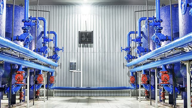 A bright room lined with corrugated metal walls containing large blue tanks and pipes