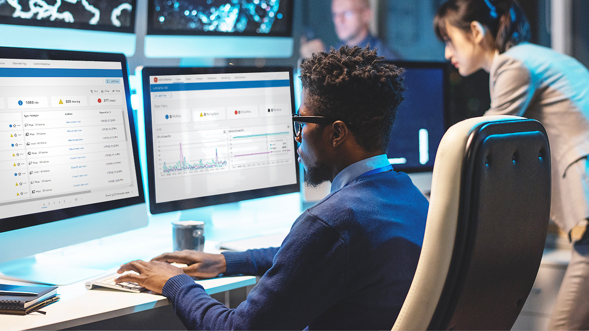 A man sitting in front of two monitors that are displaying metrics, including text and numerical data