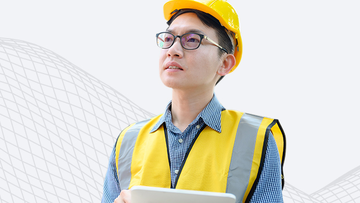 A person wearing glasses and safety gear holding a laptop and gazing upward thoughtfully
