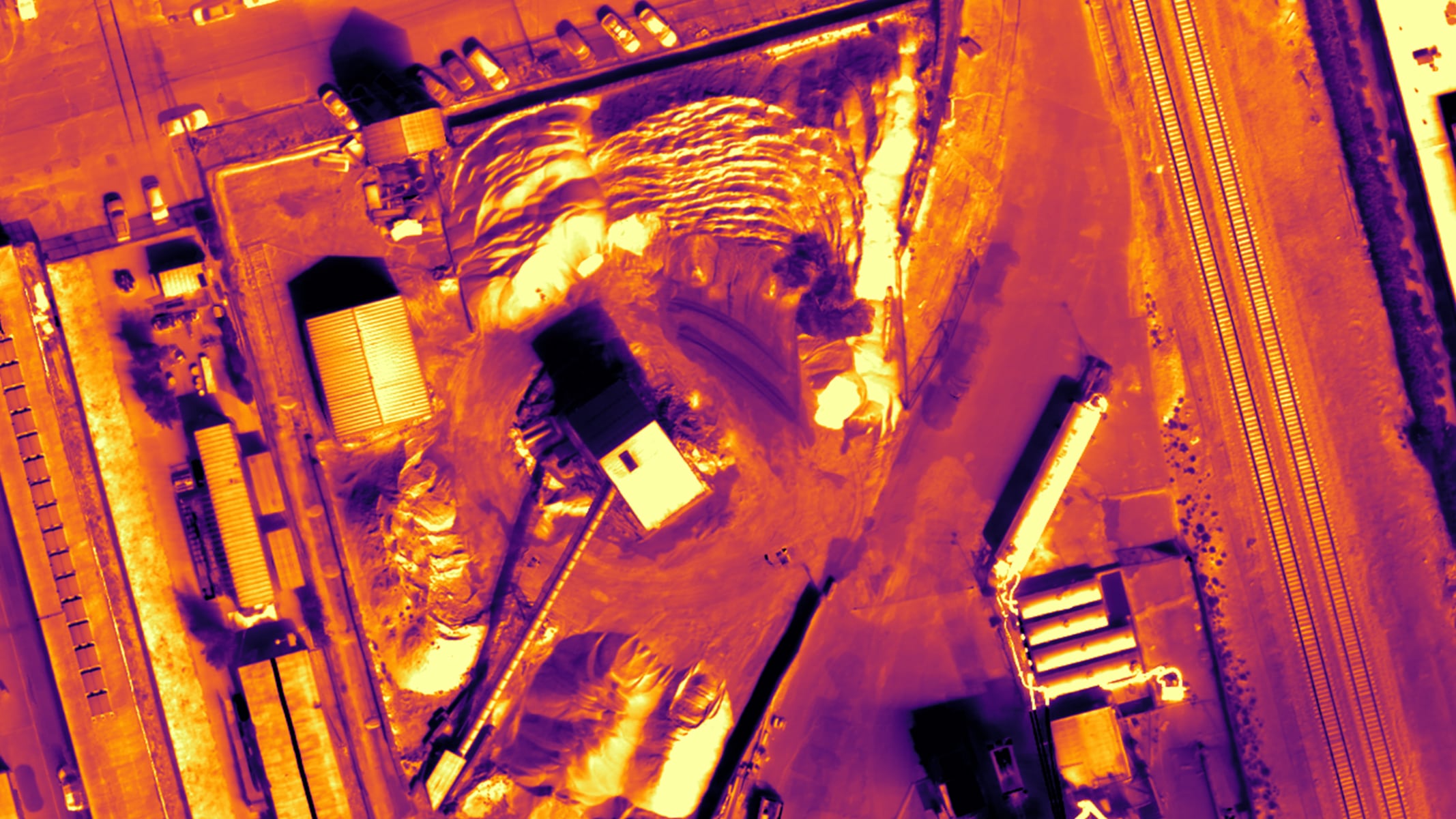 An aerial view of an asphalt plant overlaid with a heatmap layer, shading areas in purple, orange, and yellow