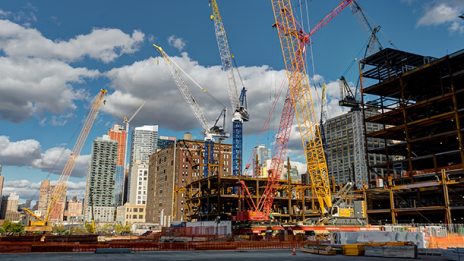A skyscraper construction site with several tall cranes under a bright blue sky with scattered clouds