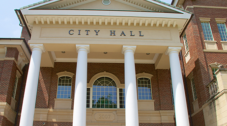 Front of a brick building with tall white columns and the words city hall on top