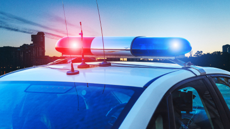 The hood of a police cruiser with flashing red and blue lights under a blue sunset sky