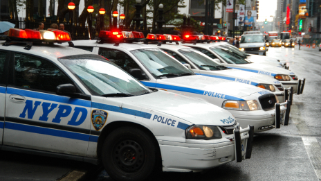 A row of white and blue NYPD cruisers parked on a rain-washed city street