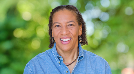 Portrait of Dr. Dawn Wright smiling in a blue chambray collared shirt with sun-dappled trees in the background