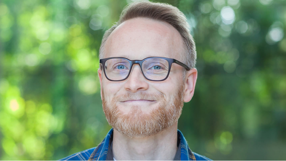 John Nelson smiling in front of green foliage in soft focus