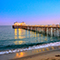 People walking and dining on a pier that stretches into the ocean at dusk