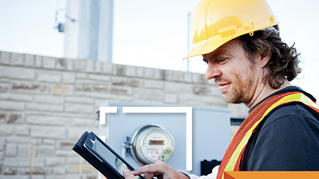 Person in a hard hat standing in front of a meter board, looking at a tablet.