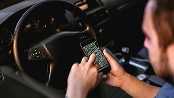 A person in the driver’s seat of a car accessing a map on a mobile phone