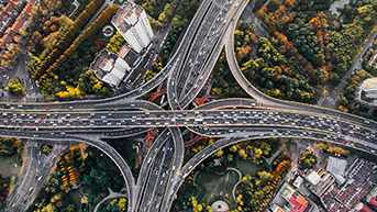 An aerial photo of a busy highway interchange in a tree-filled urban setting in autumn colors