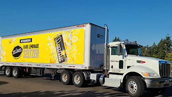 A big rig truck bearing a bright yellow ad on the side parked under a clear blue sky