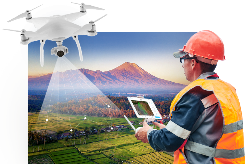 Drone pilot wearing an orange hard hat and vest flying a drone in a green field with mountains