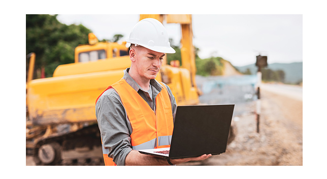 Arbeiter mit Laptop auf einer Baustelle mit Planierraupe im Hintergrund