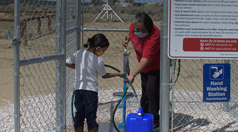 A parent and child at a safe water site filling a container with water