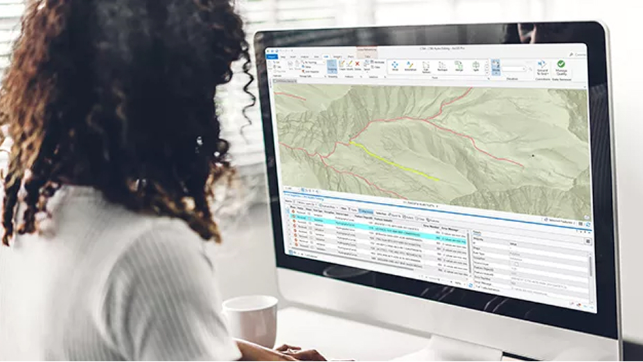 A person using a large desktop computer screen displaying a map and a table of data