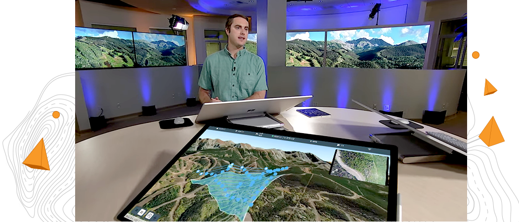 Man standing at a large round table in front of a large computer monitor with 2 large TV monitors showing a digital 3D image