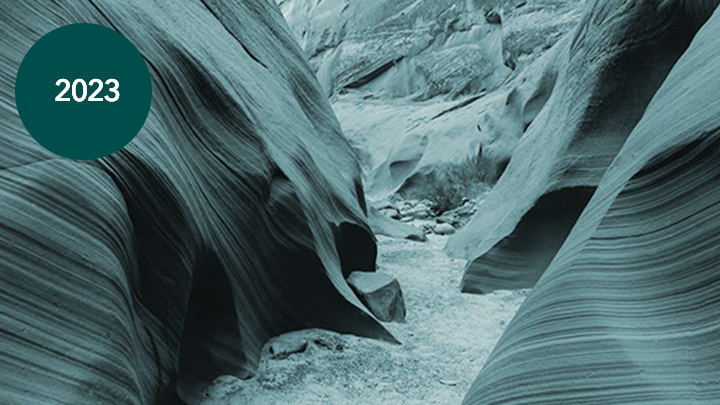 A photo of a winding path through a natural rock formation of smooth, flowing striated stone in shades of deep aqua and black