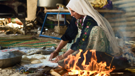 A person rolls bread dough on the ground by an open fire