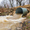 A hillside storm drain gushing with brown water  