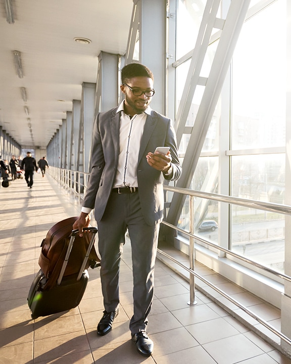 A young man in an airport looking at a phone and an image of a blue digital map with routes highlighted in red and yellow