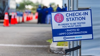 A street lined with orange cones and group of workers wearing blue shorts next to a sign that says check-in station