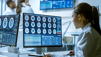 A medical tech in a white lab coat looking at brain scans on a computer monitor