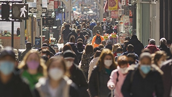 A crowded city sidewalk with people walking and wearing face masks