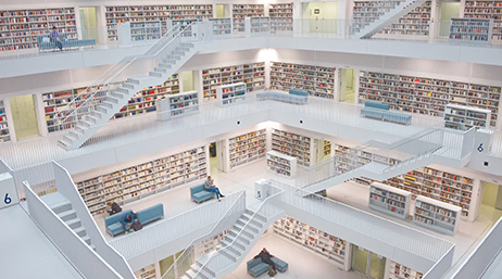An interior view of a four-story modern library in pale tones with sleek blue furniture and many bookcases full of colorful books