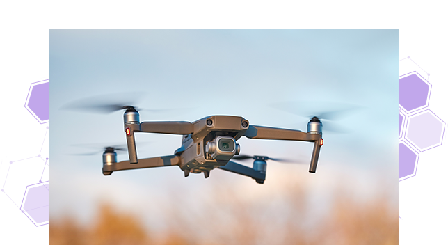 A closeup photo of a drone in flight over a field of dark yellow wheat against a pale blue sky