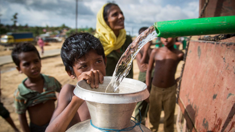 Rohingya refugee boy and others waiting for water as it is dispensed into a container