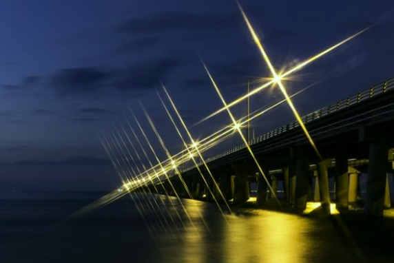 A bridge that crosses a body of water illuminated by streetlights 