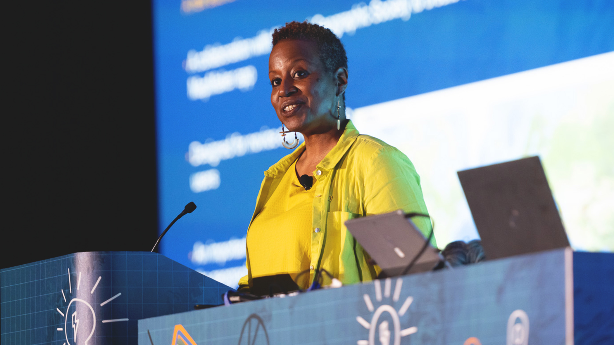 Conference presenter stands at a podium and looks out over the audience