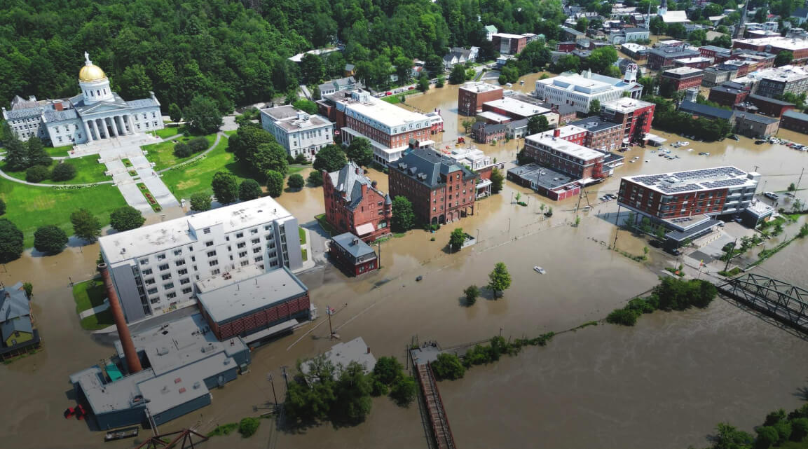 Floodwaters partially submerging a Vermont town with brick buildings and lush greenery