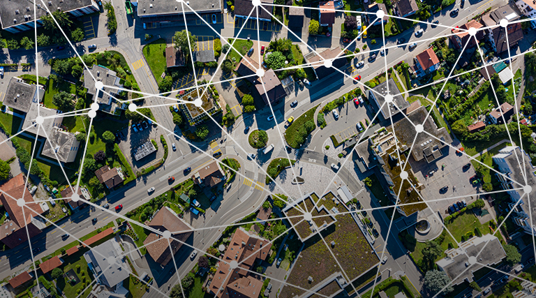 Aerial view of an urban neighborhood with roads, buildings, and greenery overlaid with a white network graphic.