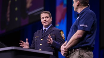 Uniformed presenter from the Washington, DC fire department gestures while turning towards another person onstage