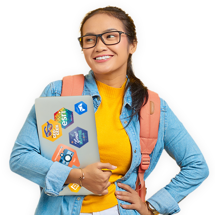 Conference attendee wearing glasses smiles while holding a laptop decorated with Esri stickers
