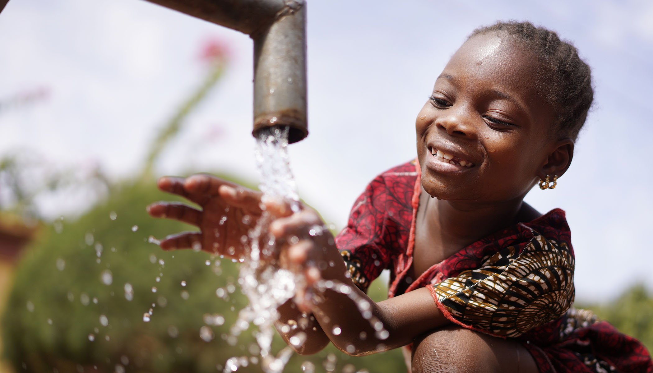 Criança sorrindo com as mãos na água saindo de uma torneira