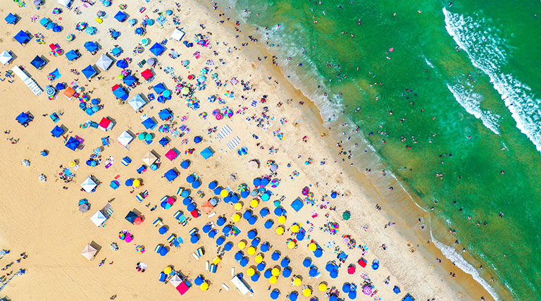 Aerial view of a crowded beach with colorful umbrellas and waves along the shoreline