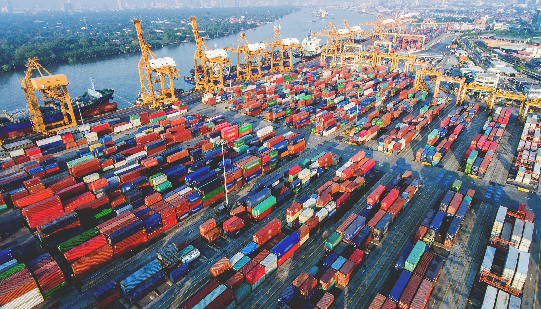 A seaport with yellow cranes at the docks and stacks of blue, red, white, and green shipping containers