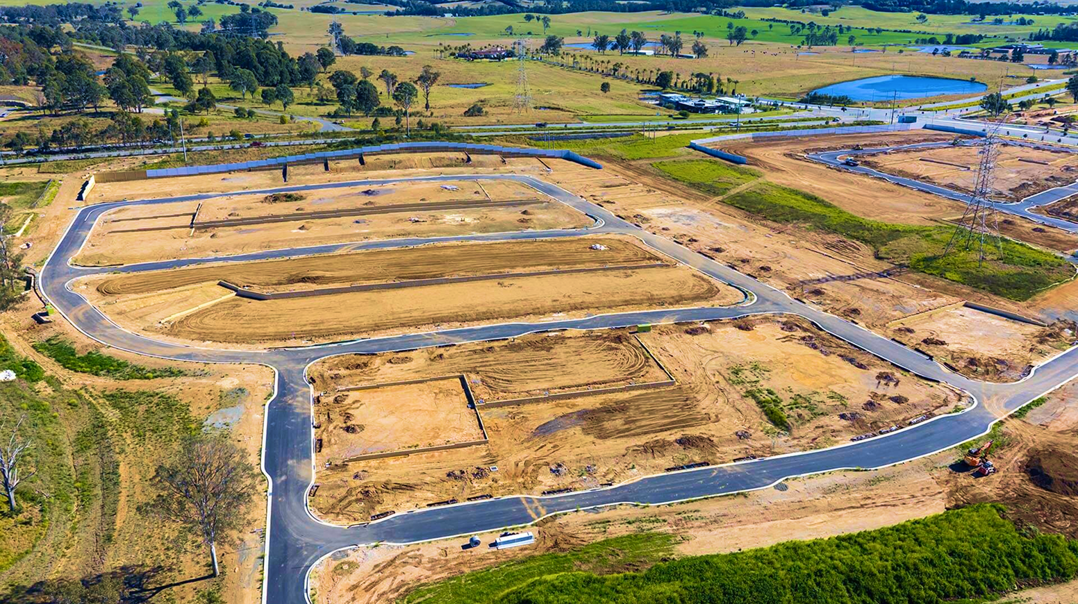 Aerial view of a land development site with graded lots and winding roads bordered by green fields