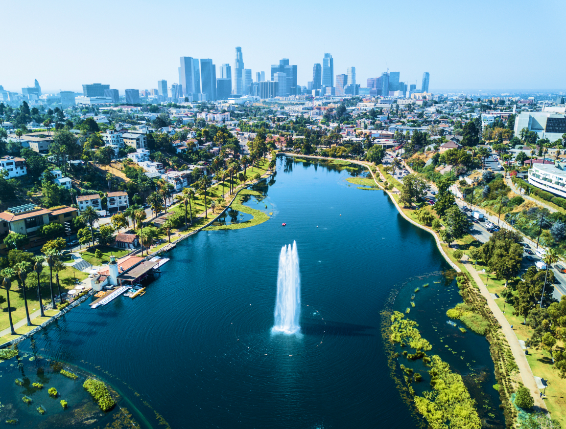 Gemeinde an einem künstlich angelegten See mit Palmen und Grünflächen mit der Skyline von LA im Hintergrund