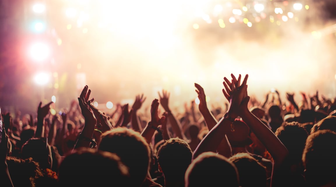 A huge crowd raises their hands in celebration in front a brightly lit stage during a concert