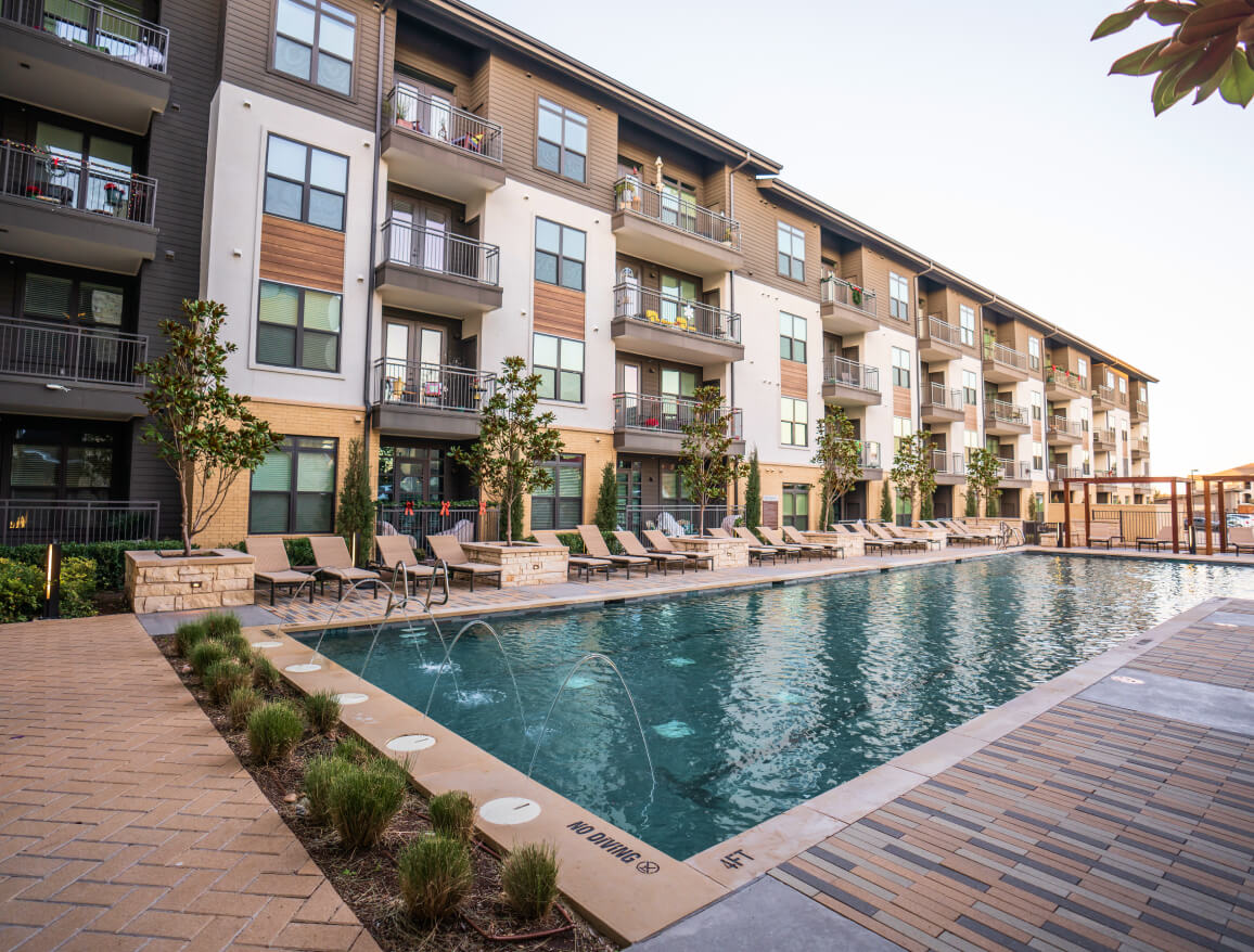 A beautiful Marriott pool area with greenery and lounge chairs and a four-story hotel with balconies
