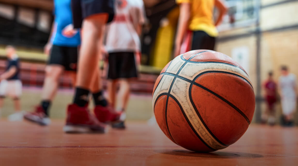 Ein Basketball auf einem Platz mit Trainer und Basketballspielenden im Hintergrund